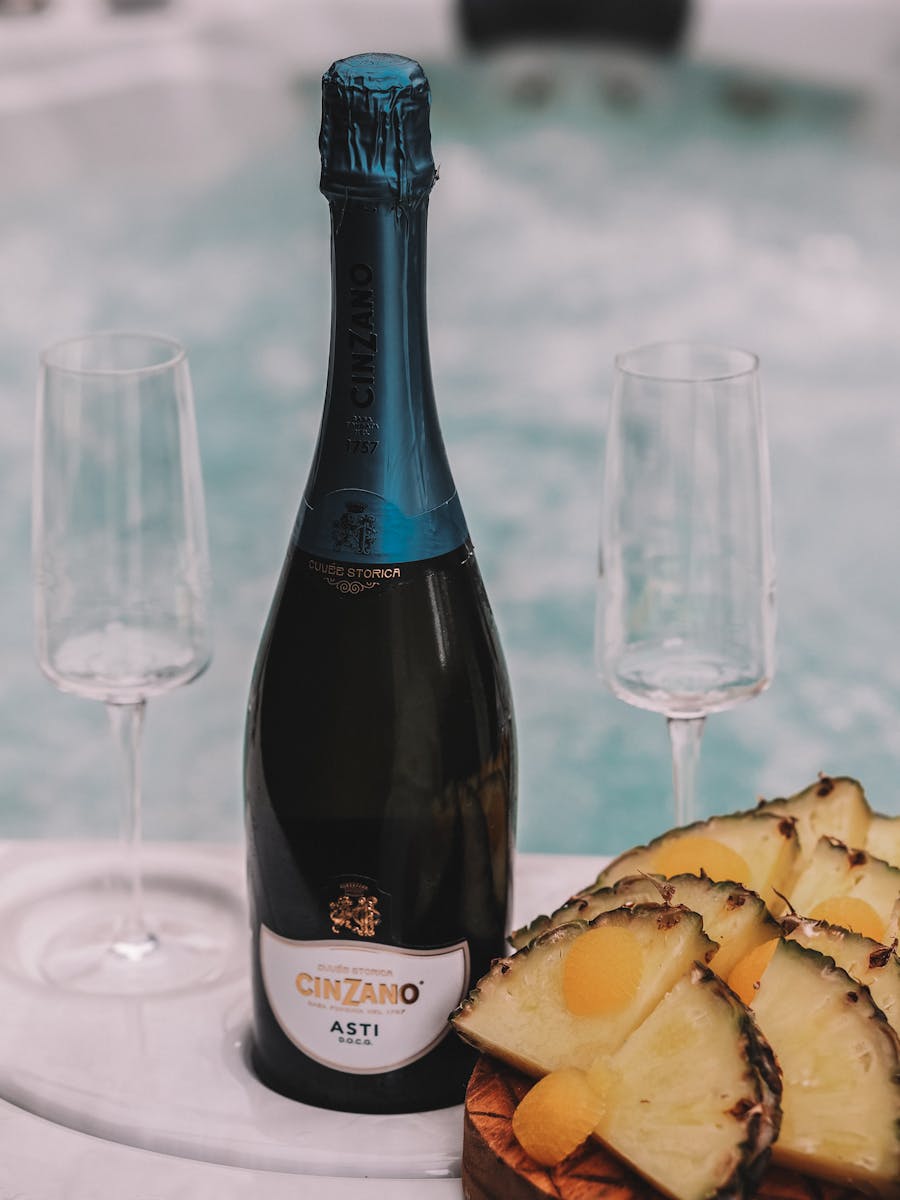 Close-up of a Cinzano Asti bottle with pineapple slices and empty wine glasses on a table.