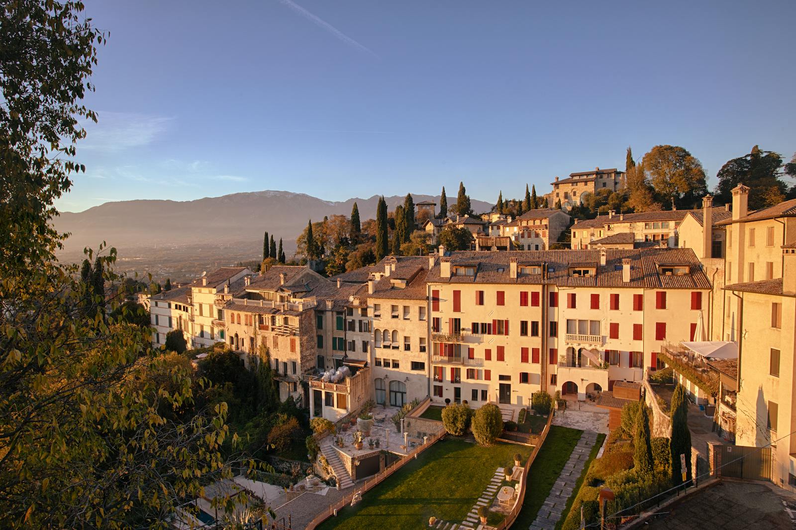 Picturesque view of Asolo, Italy with charming hillside architecture and vibrant sunset hues.